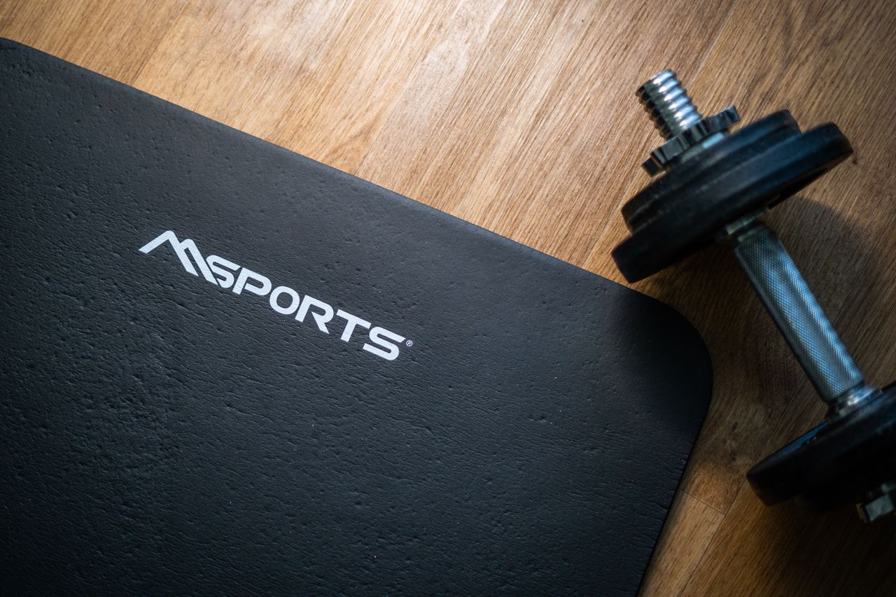 services-01 Flat lay of a gym mat and dumbbell on wooden floor, ideal for indoor workouts.