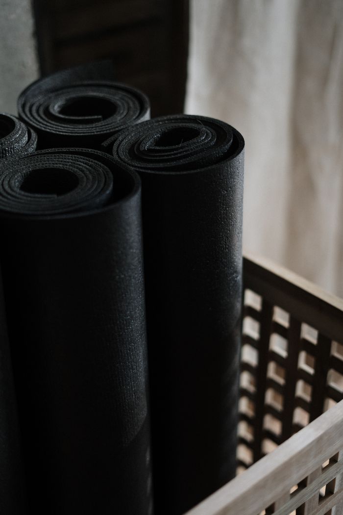about-01 Close-up view of black yoga mats rolled and stacked in a wooden basket indoors.