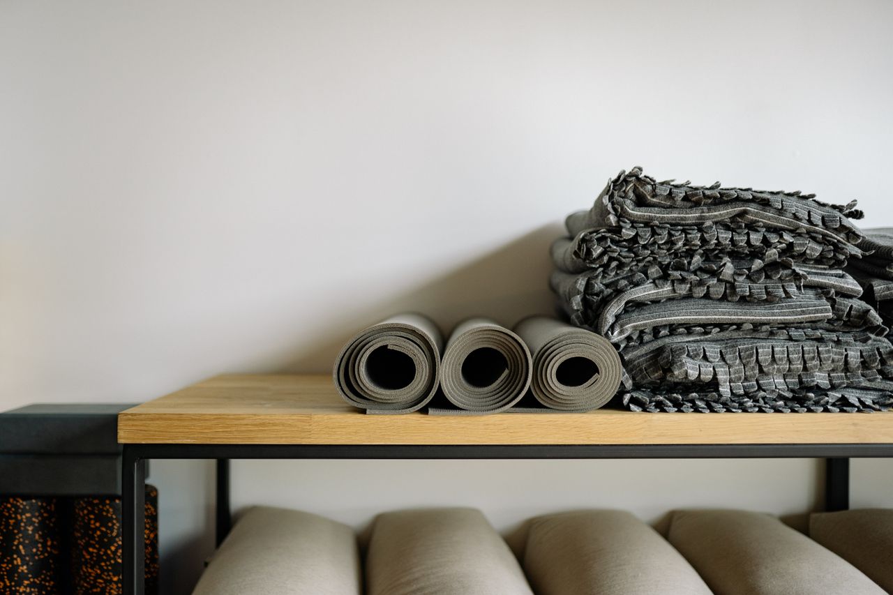 why-choose-us Neatly arranged yoga mats and blankets on a shelf in a serene yoga studio setting.